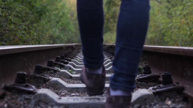 Female legs walk along train tracks