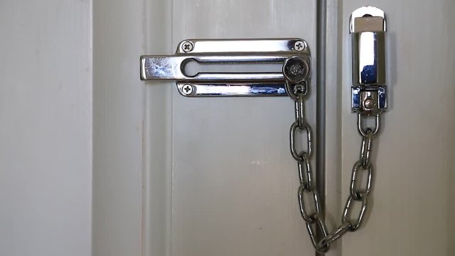 Woman moves safety chain to open the door. Woman hand and door safety chain