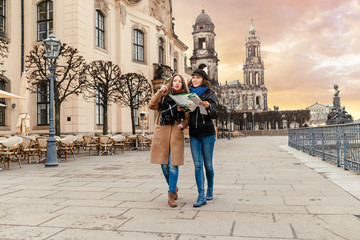 Two charming cheerful women are walking with a map along Dresden Street, Germany. The concept of...