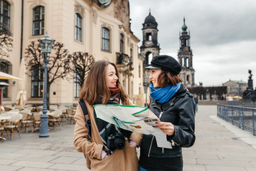 Two charming cheerful women are walking with a map along Dresden Street, Germany. The concept of...