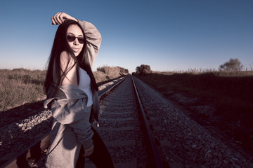 Joven con gafas de sol caminando por las vías del tren