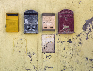 Old metal mailboxes on a grungy yellow wall.