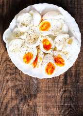 Hard boiled eggs, sliced in halves with black pepper spice on wooden background top view