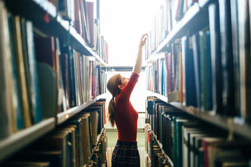 Woman taking book from library bookshelf