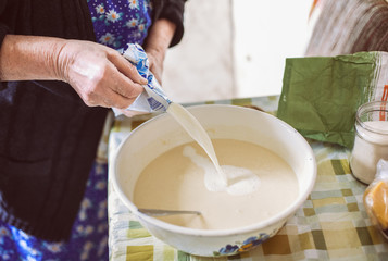 Obraz na płótnie Canvas Grandmother pouring milk into pancake batter