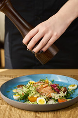 Vegetable salad with cucumber, lettuce, cherry tomatoes, salmon and eggs. Woman waitress pepper dish