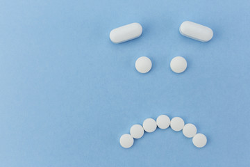upset face made by pills on blue background