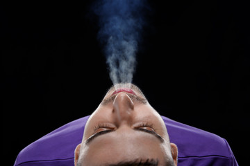 Young man exhaling smoke on black background