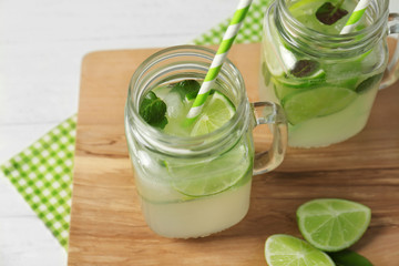 Glass jars of bracing cocktail with lemon slices and mint leaves on wooden board