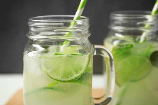 Glass jars of bracing cocktail with lime slices on dark background, closeup