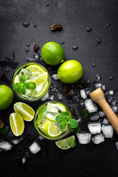 Refreshing mint cocktail mojito with rum and lime, cold drink or beverage with ice on black background, top view