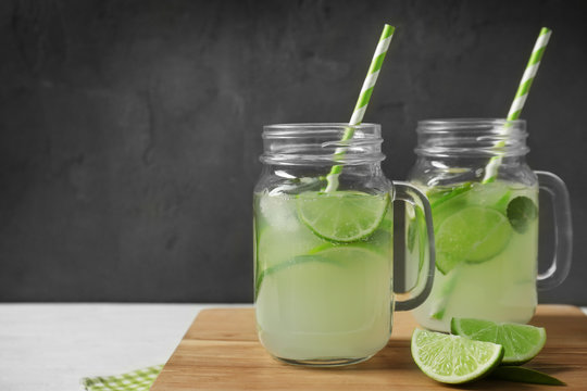 Glass jars of bracing cocktail with lime slices on wooden board against dark background