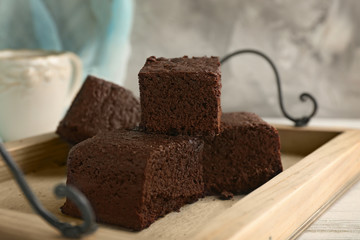 Wooden tray with pieces of delicious chocolate cake on table