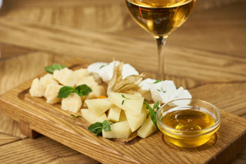 Cheese plate with mozarella, parmesan, honey and glass of white wine.