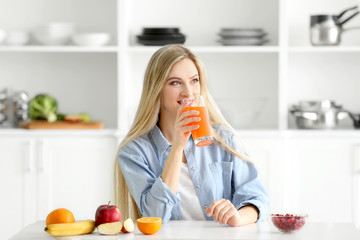 Obraz na płótnie Canvas Beautiful young woman drinking fresh juice in kitchen