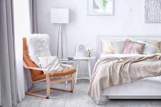 Chair near comfortable bed with soft beige coverlet and pillows in light modern room