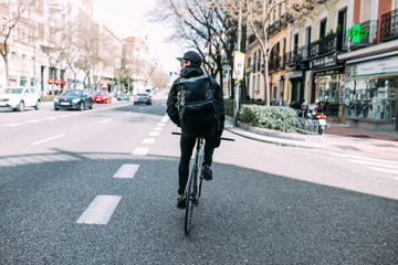 male Messanger riding fixed gear fixie bicycle around urban city of barcelona, spain with large black backpack bag making deliveries in soft light