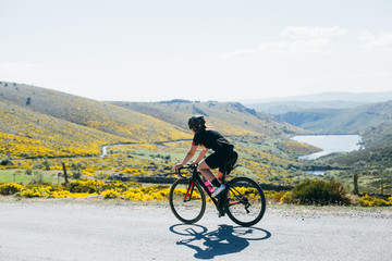 Female cyclist dressed in all black riding bicycles through the green and yellow rolling hills long shade and bright white light.