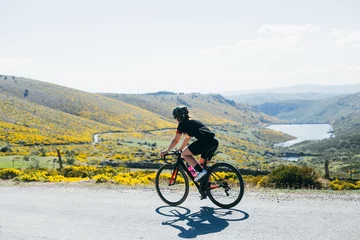 Washable wall murals Bicycles Female cyclist dressed in all black riding bicycles through the green and yellow rolling hills long shade and bright white light.