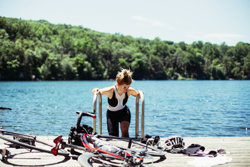 female blonde cute skinny cyclist makes a break from super hot summer bicycle ride to swim in a bright blue lake with bikes laying on dock.