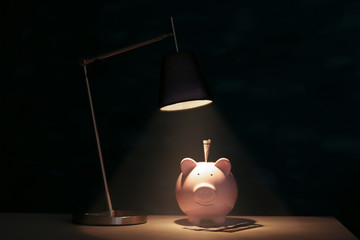 Cute pink piggy bank on illuminated surface under lamp