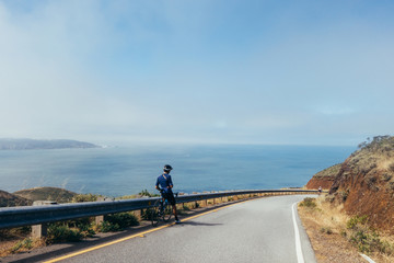 Group of cyclists, teammates, friends, descending windy narrow road next to the bay with fog and water and blue skys san francisco in norhtern california.