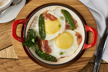 bacon and eggs with green peas in red pan served on wooden table in restaurant