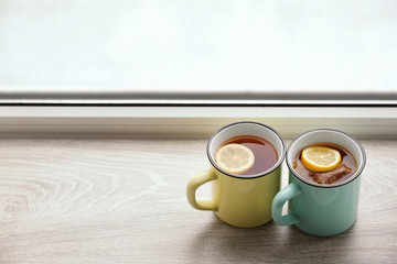 Cups of hot tea with lemon on window sill
