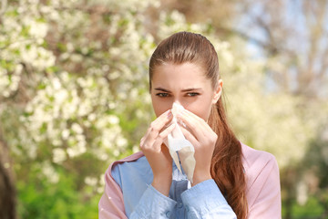 Sneezing young girl with nose wiper among blooming trees in park