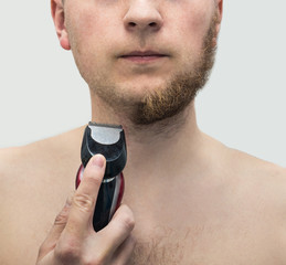 Young hipster man shaved half of his ginger beard with electric shaver machine