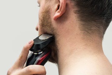 Back view of young hipster man shaving his ginger beard off with an electric shaver. Back view