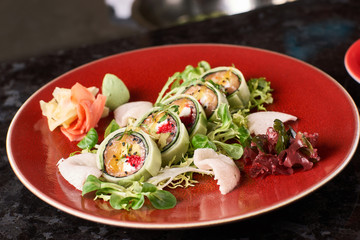 Sushi roll with salmon, avocado, tuna fish, sesame and cream cheese served on red plate with fresh lettuce on black marble background