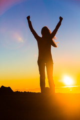 Winner woman winning with open arms in success of reaching mountain top in sunset flare, goal...