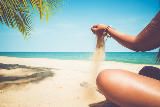 Relaxation and Leisure in Summer lifestyle image of slim tanned girl on beach, pours a sand in hand. On hands many seashell bracelets. Tropical island beach