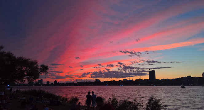 Silhouetted couple and other onlookers admiring a brilliant colorful sunset over the Charles River on the Esplanade in Boston on July 3rd, 2016