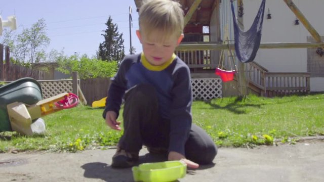 Adorable kids flips toy frog into a bucket in his backyard on a sunny day
