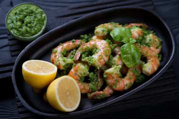 Close-up of a frying pan with tiger shrimps served with parsley sauce and lemon, selective focus