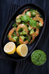 Tiger shrimps with parsley sauce and lemon in a frying pan over black wooden background, studio shot