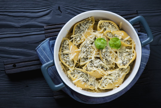 Baked conchiglioni stuffed with cottage cheese and spinach over black wooden background, high angle view, horizontal shot