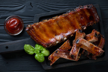 Black wooden serving tray with oven baked pork ribs glazed in soy sauce and honey, above view, studio shot