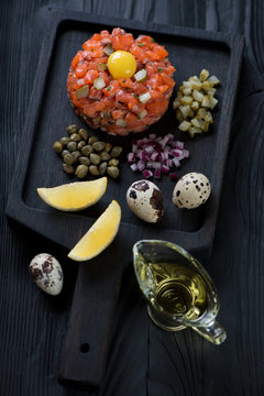 Black wooden serving tray with salmon tartare, vertical shot, selective focus