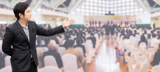 businessman standing welcome with abstract blurred of conference hall or seminar room with attendee or audience background.