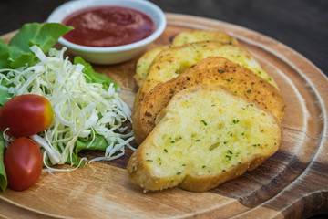 Garlic bread and vegetable salad on wooden cutting board
