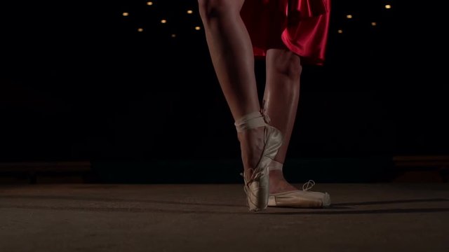Close-up of ballerina legs in red dress and Pointe shoes on the stage.