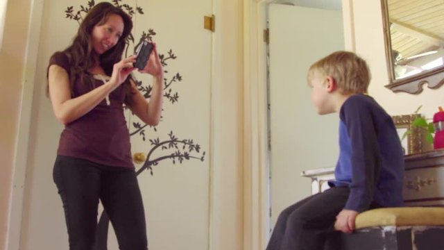 Attractive mother photographs adorable little boy acting silly using her cell phone 