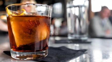 Fototapeten Cocktail hautnah. Bar oder Restaurant mit verschwommenen Menschen im Hintergrund. Trinken Sie mit einem einzigen großen Eiswürfel. © Crin