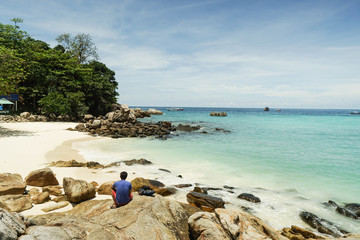 man sit on rock at shore with clear blue sea for relaxing in holidays