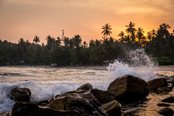 Wellen brechen am Strand und im Hintergrund der Sonnenuntergang