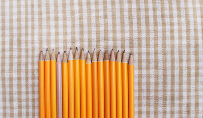 Brown pencil among Orange pencils on table