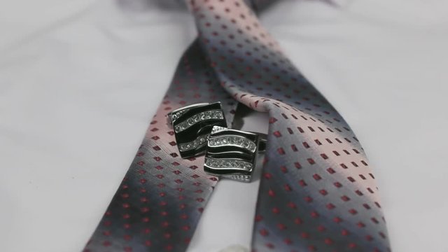 Dolly shot. Close-up knotted pink tie and cufflinks on a white shirt.